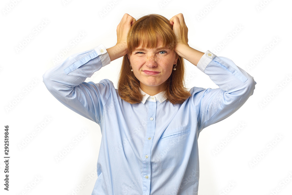Young girl with ginger hair and freckles touching her head as having a headache our feeling tired, overwhelmed with noises. White background, copy space, isolated model. Young girl with ginger hair and freckles touching her head as having a headache our feeling tired, overwhelmed with noises. White background, copy space, isolated model.