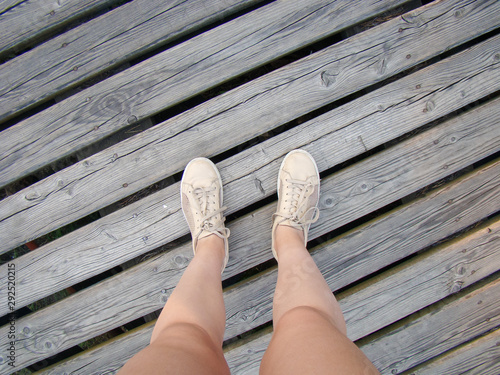 Legs of a girl in sneakers. Stands on a wooden floor at intervals. View from above.