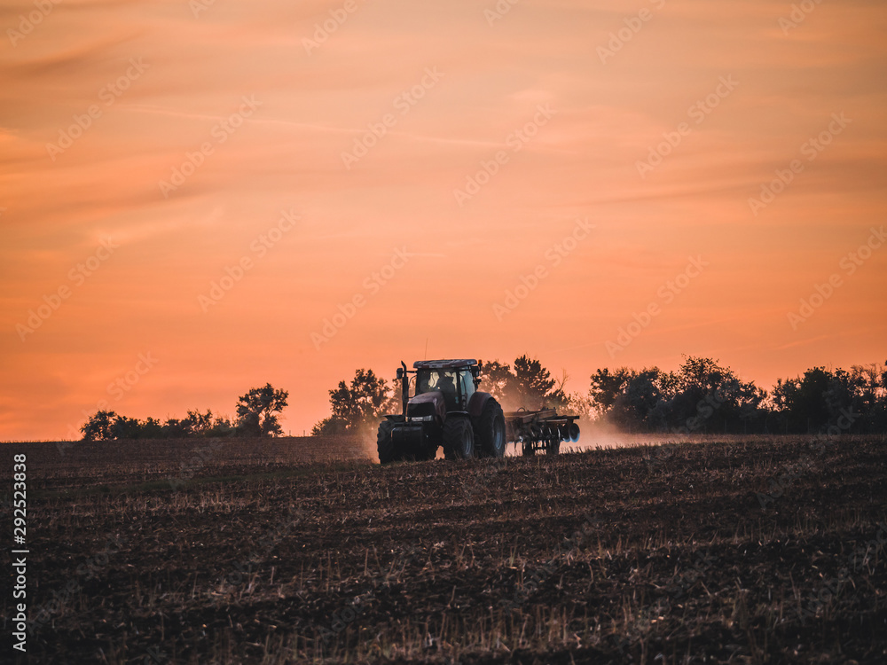 Fototapeta premium Tractor on filed by sunset.