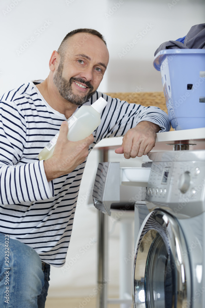 Obraz premium man loading clothes into washing machine in kitchen