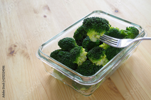 Steamed boiled broccoli on a fork in a glass container on a wooden background with copy space. Proper nutrition, super food and fitness