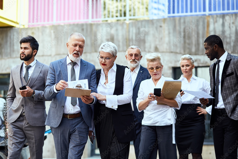 Seven businessman walking down the street and discussing project. Five of them blond, two brunettes Seven businessman walking down the street and discussing project. Five of them blond, two brunettes