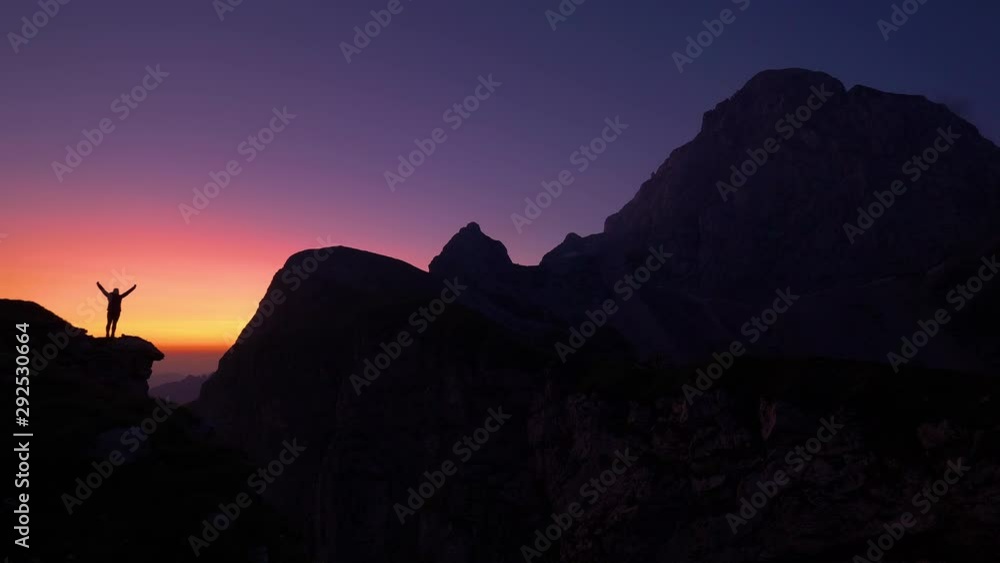 SLOW MOTION, COPY SPACE, SILHOUETTE: Cinematic shot of a cheerful hiker outstretching arms after reaching summit just before sunrise. Joyful trekker celebrates reaching the mountaintop at sunset. SLOW MOTION, COPY SPACE, SILHOUETTE: Cinematic shot of a cheerful hiker outstretching arms after reaching summit just before sunrise. Joyful trekker celebrates reaching the mountaintop at sunset.