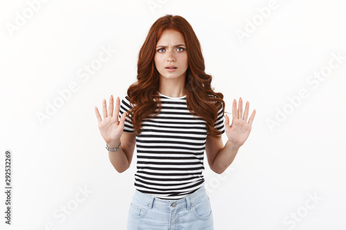 Serious-looking annoyed and disappointed young redhead woman in striped t-shirt wanna finish conversation, show raised hands in stop, rejection gesture, say no, frowning with dislike and aversion