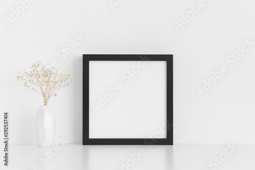 Fototapeta Makieta czarna kwadratowa ramka z gipsówką w wazonie na białym stole.