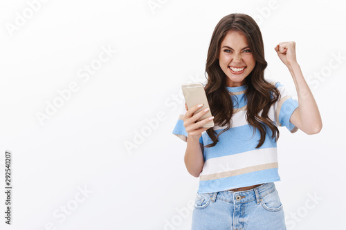 Excited joyful caucasian girl receive excellent score bit level, fist pump and celebrating perfect news, smiling rejoicing, triumphing achieve goal, winning online lottery, stand white background