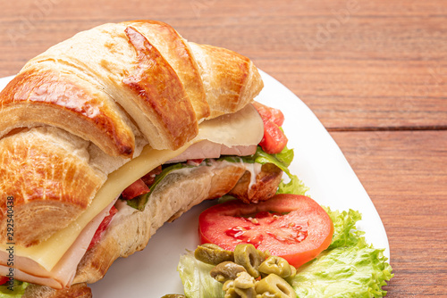 Croissant sandwich with salad, ham, cheese, tomatoes and olives on wooden background. Morning breakfast concept. Healthy and fast food. Isolated.