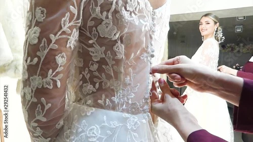 Woman helps a young bride to wear a wedding dress.