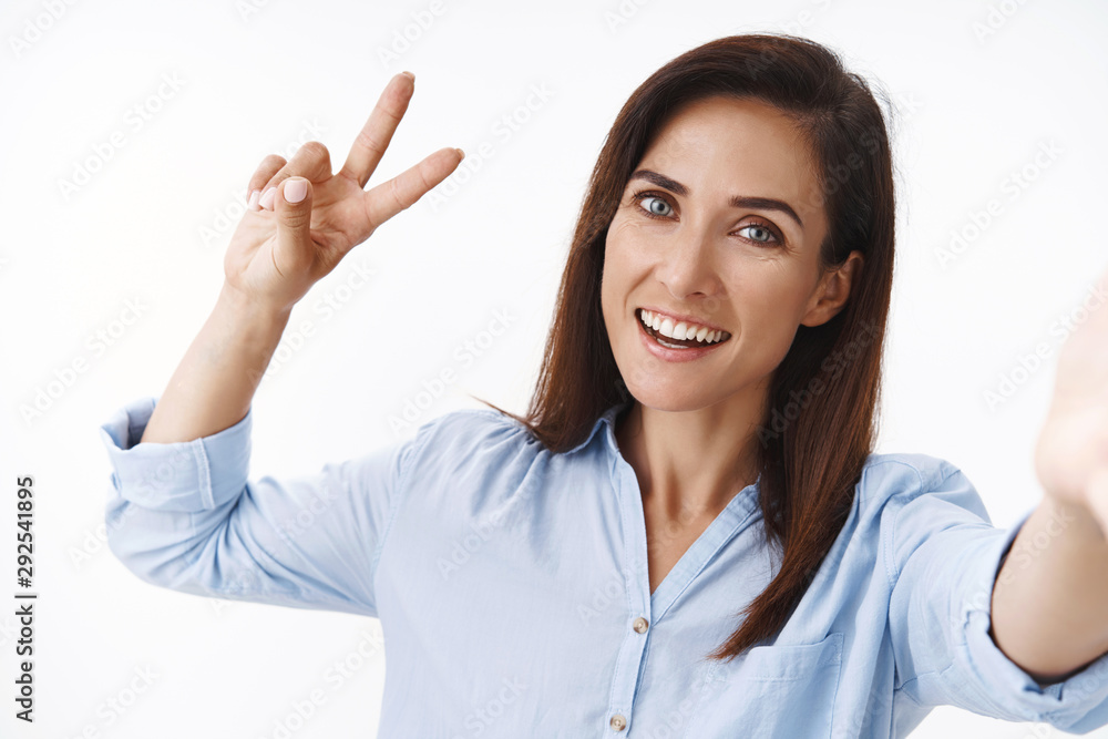 Cheerful carefree adult caucasian female 30s woman extend arm, hold camera hand, show peace victory sign, posing selfie, smiling casual relaxed expression, send hello, photographing social media Cheerful carefree adult caucasian female 30s woman extend arm, hold camera hand, show peace victory sign, posing selfie, smiling casual relaxed expression, send hello, photographing social media