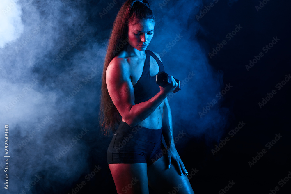 serious motivated sportswoman pumping up muscles at sport center. lifestyle. close up portrait, sexuality, isolated black background with smoke , hobby, interest