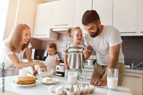 happy little adorable girl pointing her finger up talking with her daddy about recipe, while mommy looking at them and laughing photo