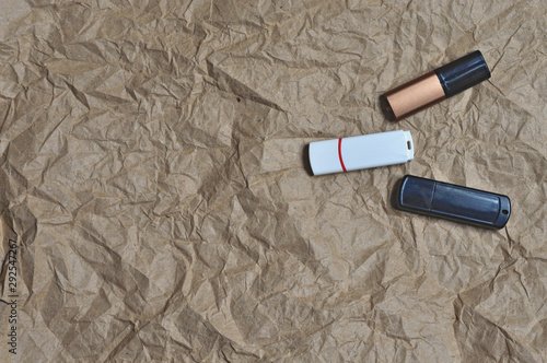 Three usb flash drives, white, black and bronze are in different positions on crumpled textured craft paper.
