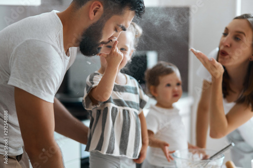 little adorable girl mussing her dad's face with flour, mother blowing flour to the husband. close up side view photo