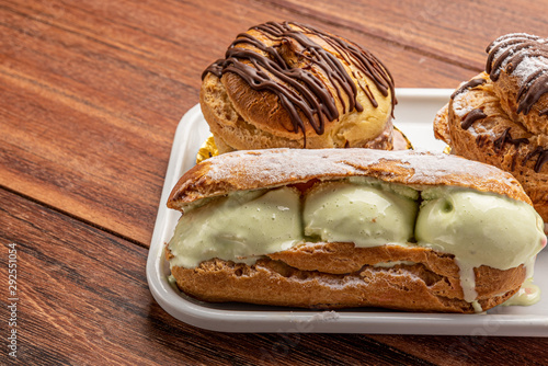 Profiteroles with ice cream and chocolate. Eclairs with black chocolate on wooden background. Traditional French dessert.