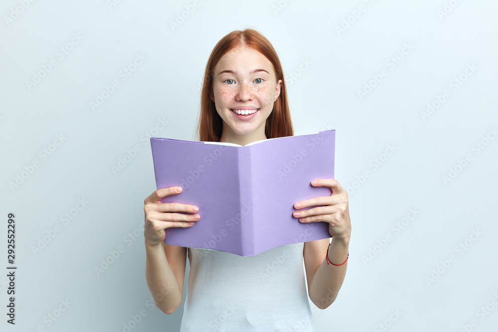 pleasant cute clever woman with freckles holding a book, reading it, student preparing for exams. close up portrait, isolated white background, studio shot pleasant cute clever woman with freckles holding a book, reading it, student preparing for exams. close up portrait, isolated white background, studio shot