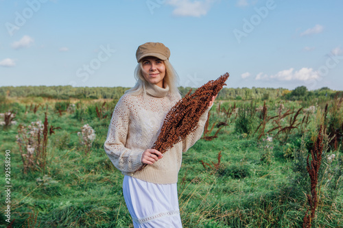Happy beautiful blond woman walking in a green field with a bouquete of dry brown plants