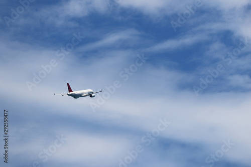 Airplane flying in the blue sky on background of white clouds, rear view. Two-engine commercial plane during the turn, turbulence and travel concept