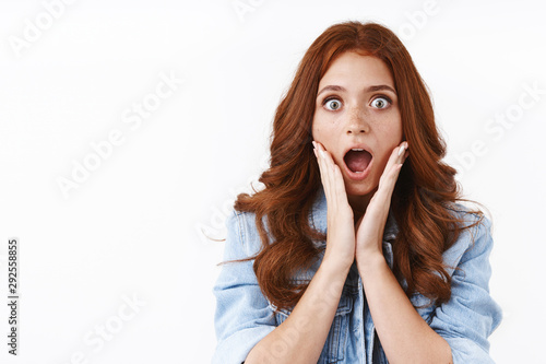 Fototapeta Close-up shocked gasping speechless young redhead woman in denim jacket, cup fac