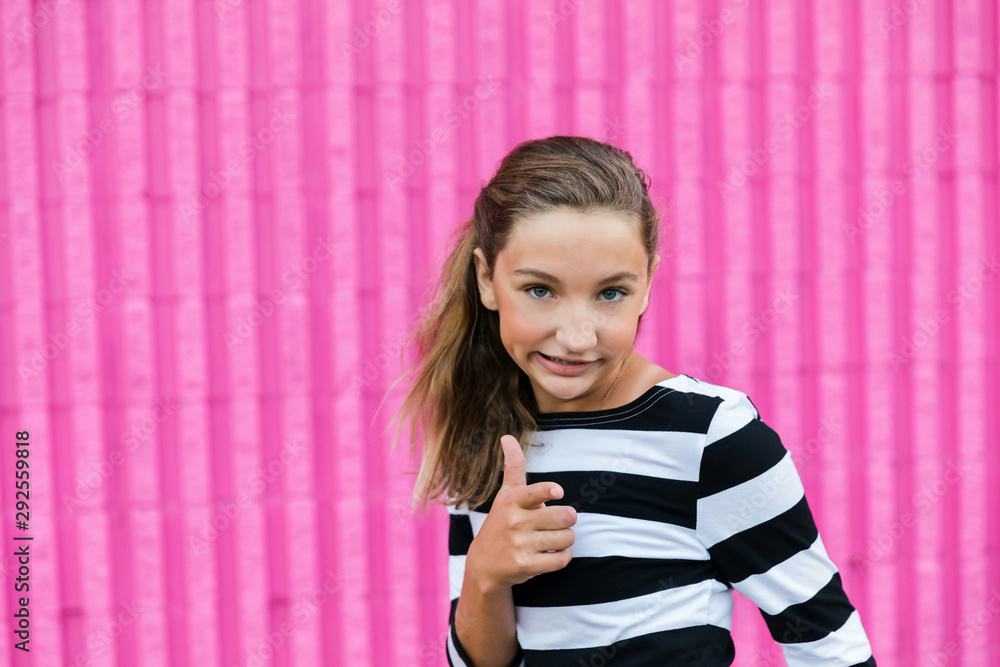 Cute caucasian girls celebrating her 13th birthday becoming a teenager in front of a hot pink wall outside making a silly face with a thumbs up sign Cute caucasian girls celebrating her 13th birthday becoming a teenager in front of a hot pink wall outside making a silly face with a thumbs up sign