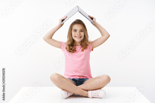 Cheerful pretty young blond child kid student, sitting amused and happy floor crossed legs, raise opened laptop under head, smiling broadly, excited studying e-learning want become programmer