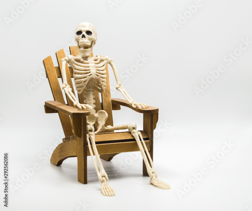 a whimsical Halloween skeleton sitting in a wooden Adirondack chair isolated on white