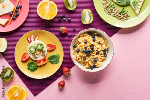 top view of plates with fancy animals made of food near fruits and breakfast cereal on purple background