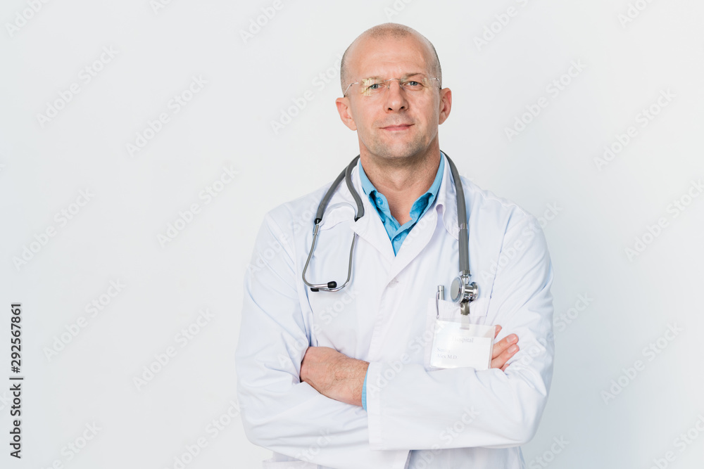 Young successful cross-armed doctor with stethoscope on neck standing by wall Young successful cross-armed doctor with stethoscope on neck standing by wall