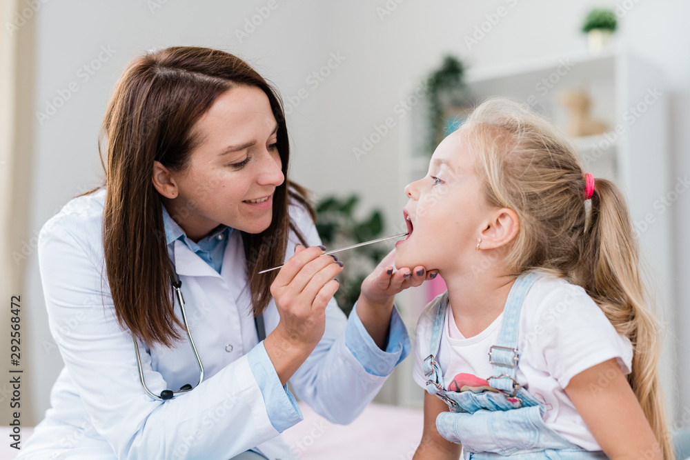 Sick little girl with open mouth while clinician examining her sore throat