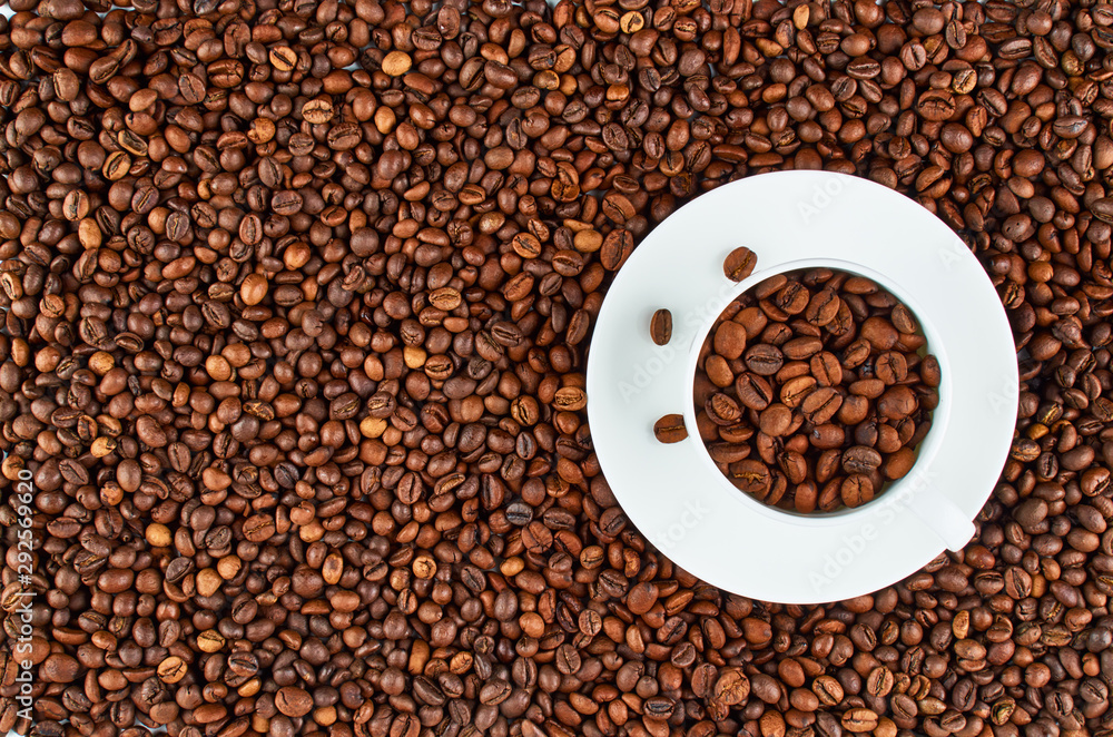 Fototapeta premium Background of roasted coffee beans. In the foreground is a white coffee Cup with coffee beans.