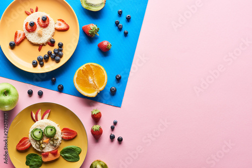 top view of plates with fancy animals made of food on blue and pink background with fruits