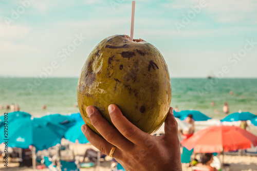 Male Hand Holding Cold Coconut On The Beach photo