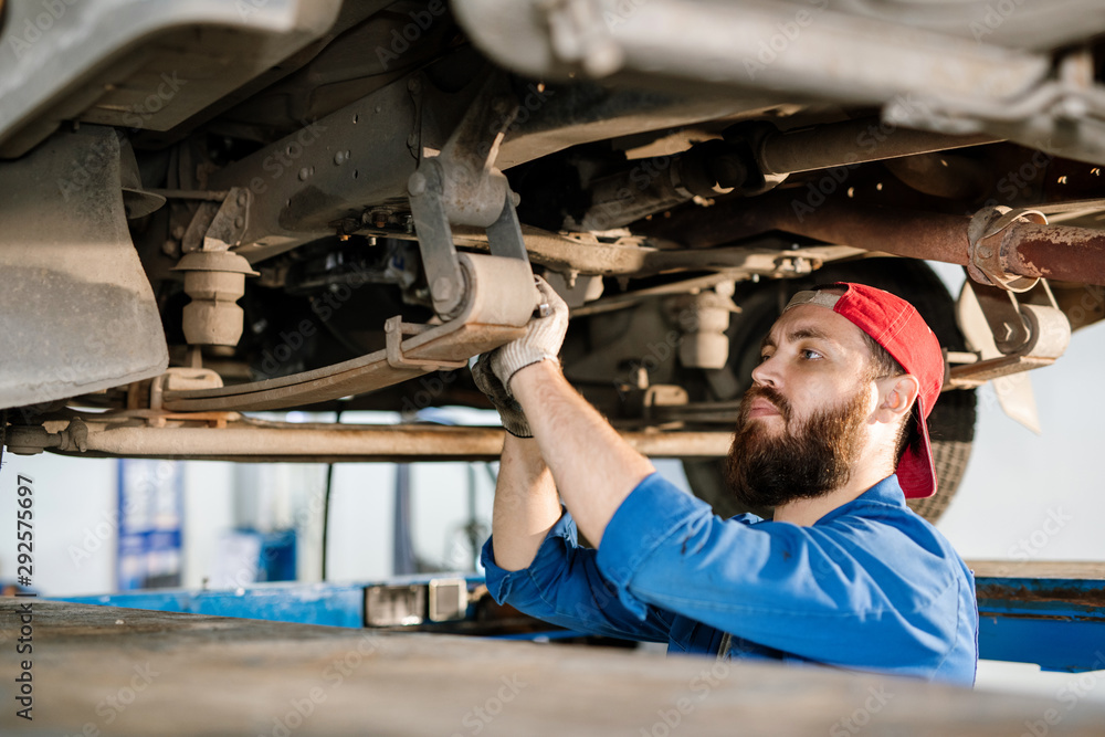 Young bearded technician of machine repair service fixing detail Young bearded technician of machine repair service fixing detail
