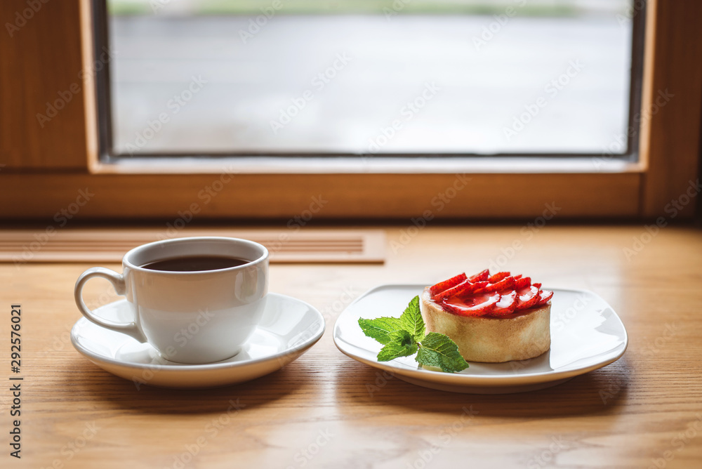 Strawberry tartlet and a cup of tea on wooden table near the window. Strawberry tartlet and a cup of tea on wooden table near the window.