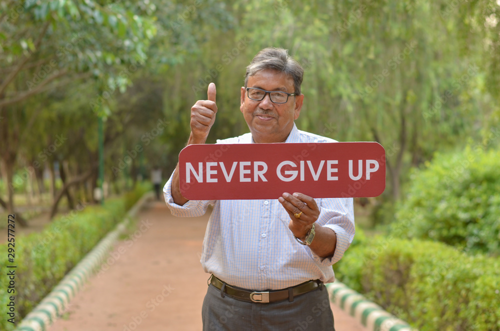 Senior Bengali Indian man holding a placard with message "Never give up
