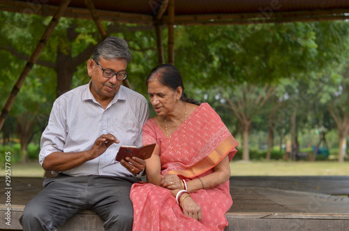 Wallpaper Mural Senior citizen Indian couple reading from mobile, smiling and laughing in the evening in a park in summer in Delhi, India. Concept love Torontodigital.ca
