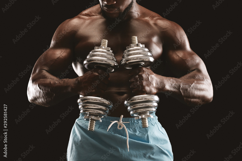 Strong athletic body of african bodybuilder holding dumbbells Strong athletic body of african bodybuilder holding dumbbells