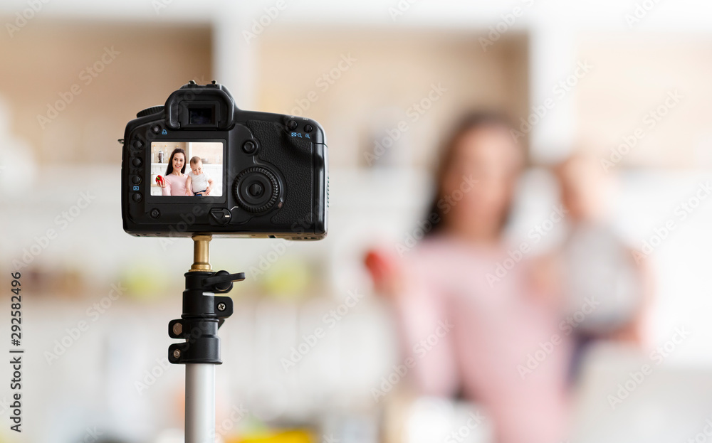 Mother with toddler recording video for webinar, kitchen interior