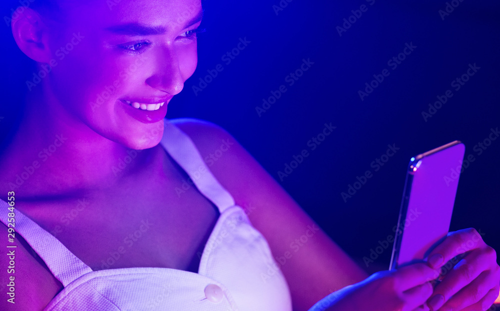 Naklejka premium Young woman using smartphone with blue and pink neon lights