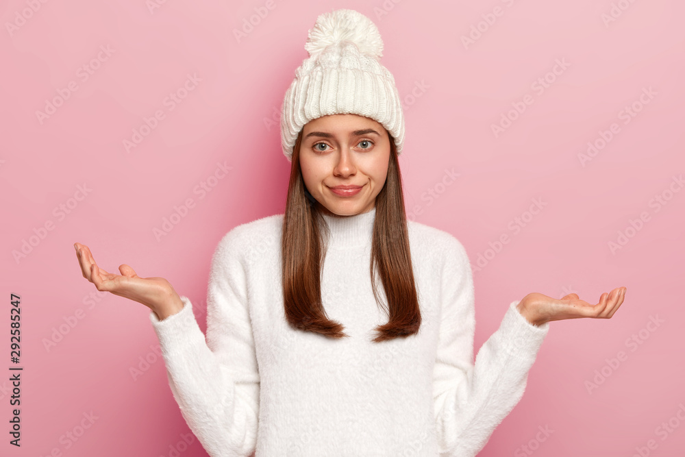 Image of hesitant European girl shrugs shoulders, being questioned what to do, looks helpless, doesnt know how to act in difficult situation, wears white hat and knitted sweater, looks confusingly Image of hesitant European girl shrugs shoulders, being questioned what to do, looks helpless, doesnt know how to act in difficult situation, wears white hat and knitted sweater, looks confusingly
