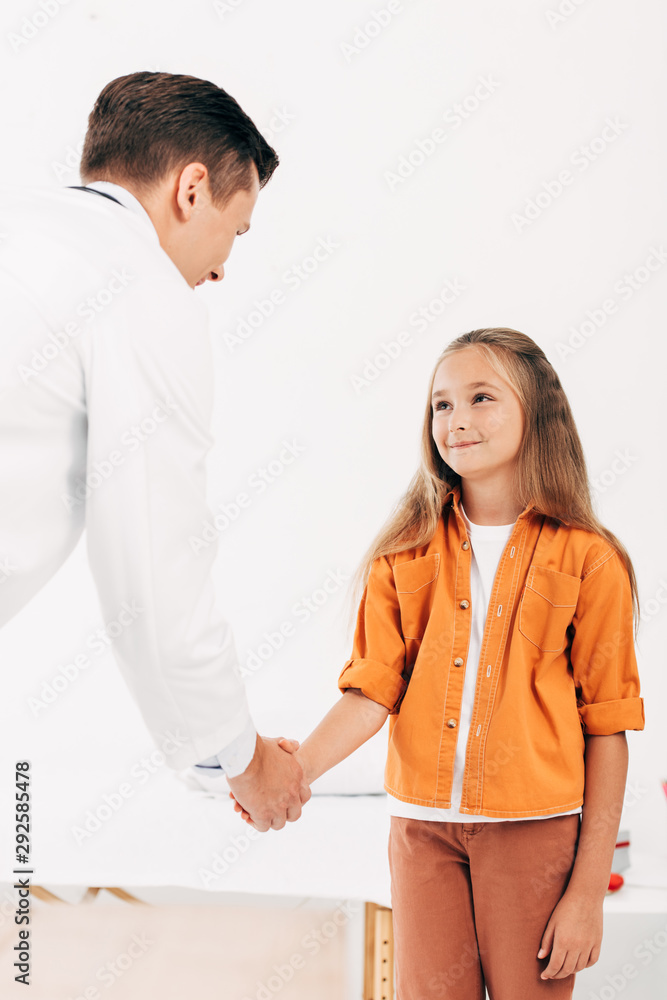 pediatrist in white coat and child shaking hands and looking at each other pediatrist in white coat and child shaking hands and looking at each other