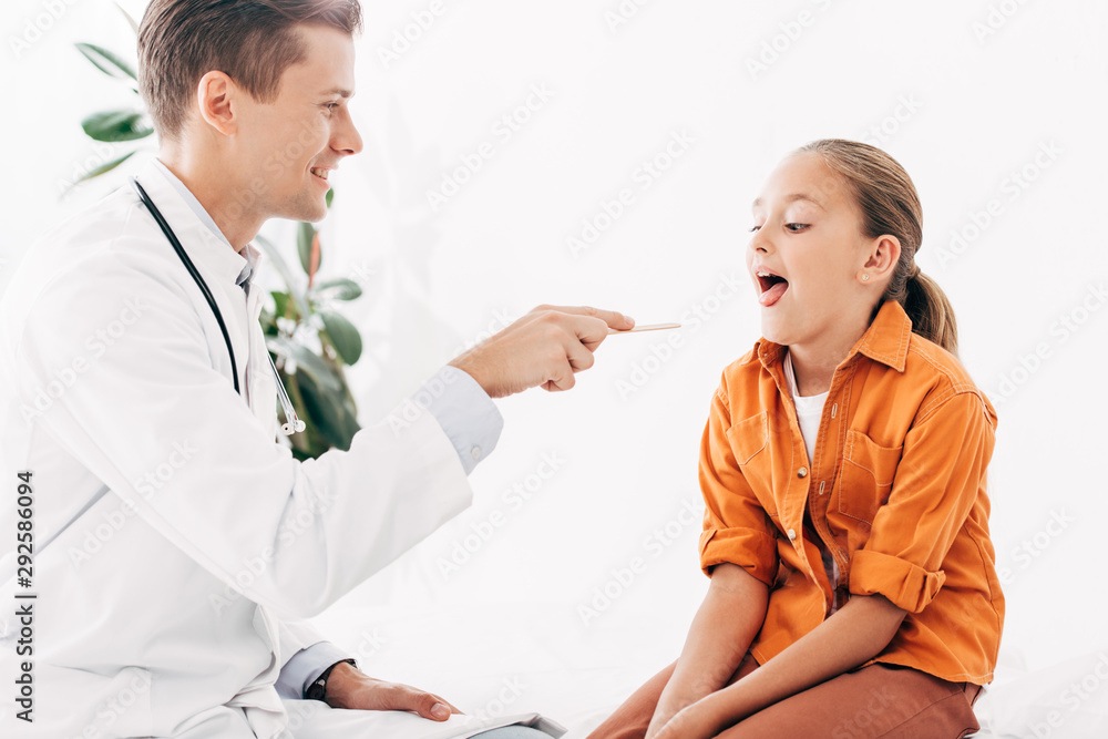 pediatrist in white coat examining child with medical spatula