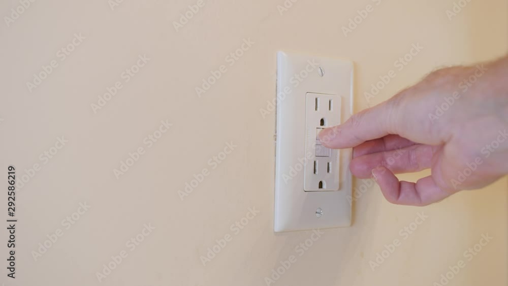 Close up of male hand resetting tripped GFI electricity receptacle. Residential ground fault interrupter electric socket plug and wall plate. Close up of male hand resetting tripped GFI electricity receptacle. Residential ground fault interrupter electric socket plug and wall plate.