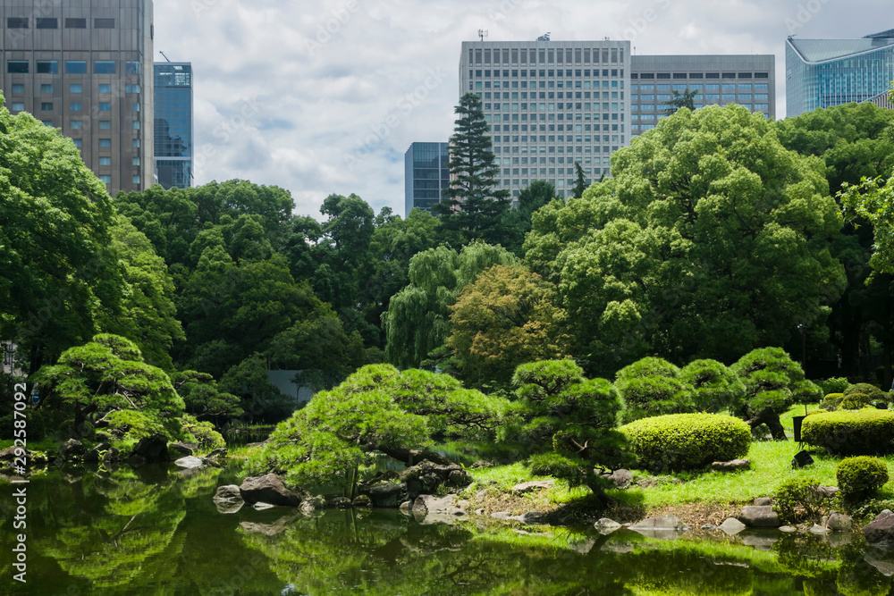 Nature or urban background with view of Hibiya park in Tokyo, Japan, with trees and tall buildings of Marunouchi business district illustrating modern urban ecology concept. Nature or urban background with view of Hibiya park in Tokyo, Japan, with trees and tall buildings of Marunouchi business district illustrating modern urban ecology concept.