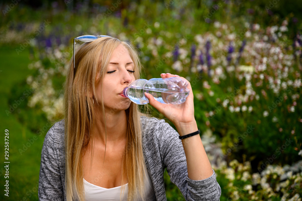 Fit woman drinking water from a bottle in a park or garden in London, England Fit woman drinking water from a bottle in a park or garden in London, England