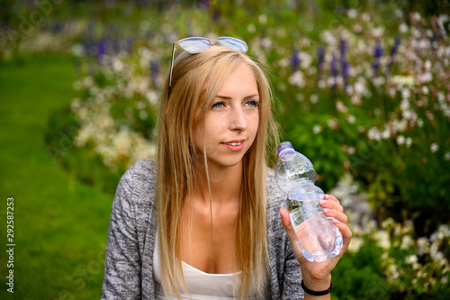 Fit woman drinking water from a bottle in a park or garden in London, England