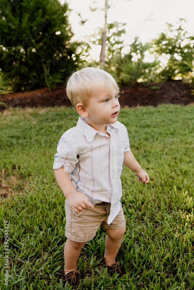 Portrait of Cute Handsome Blond Little Kid Boy in Colorful Striped Button Down Shirt Walking Outside in the Grass Watching the Sunrise Portrait of Cute Handsome Blond Little Kid Boy in Colorful Striped Button Down Shirt Walking Outside in the Grass Watching the Sunrise