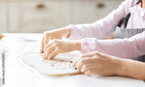 Girl cutting out cookies of raw dough on kitchen table