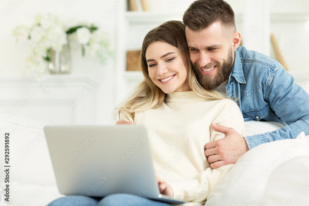 Beautiful young couple relaxing in living room and using laptop Beautiful young couple relaxing in living room and using laptop