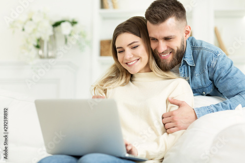Beautiful young couple relaxing in living room and using laptop © Prostock-studio