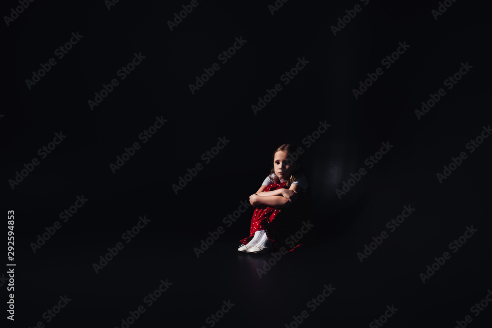 scared, lonely child sitting on floor on black background with copy space scared, lonely child sitting on floor on black background with copy space